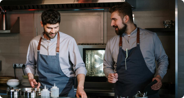 Two chefs in a modern kitchen wearing aprons, collaborating while preparing food, illustrating teamwork for launching Virtual Dining Concepts.